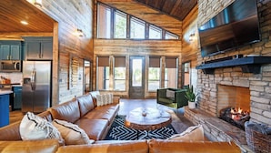A spacious living area with a stone fireplace, leather sofa, and a large TV mounted on the wall.
