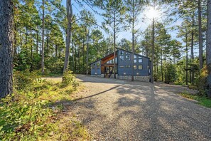 En modern stuga med en grund av sten, stora fönster och en träveranda, omgiven av ett skogsområde.