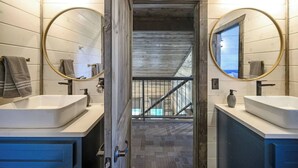 A modern bathroom with two sinks, large mirrors, and a view of a wooden staircase leading to a balcony.