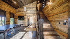 A wooden interior with a ping pong table, a foosball table, and a staircase.