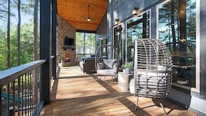 A wooden deck with wicker chairs and a stone fireplace.