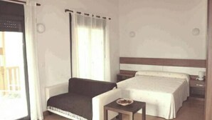 Una habitación de hotel con cama, sofá, una mesita y ventana con cortinas.