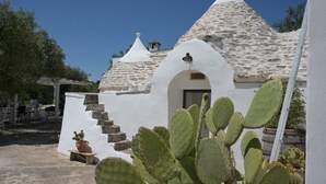 A white building with a conical roof and a small bell tower, surrounded by cacti and outdoor furniture. - Trullo Rora' - Ostuni (Puglia)