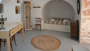 A room with a round woven rug, a wooden chair, a sofa with striped cushions, and a cabinet. - Trullo Rora' - Ostuni (Puglia)