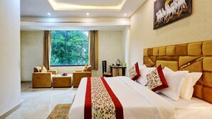 A hotel room with a large bed, a sofa, a desk, and a window with a view of trees. - Hotel Golden Era (Noida)