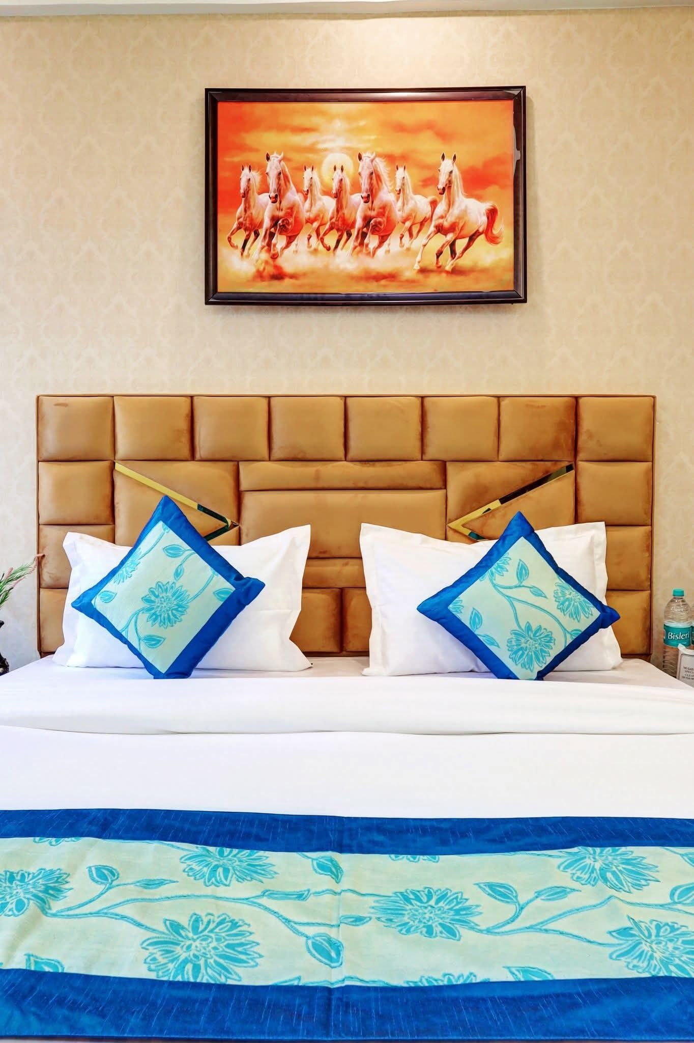 A hotel room with a large bed, a headboard, and a painting of horses on the wall.
