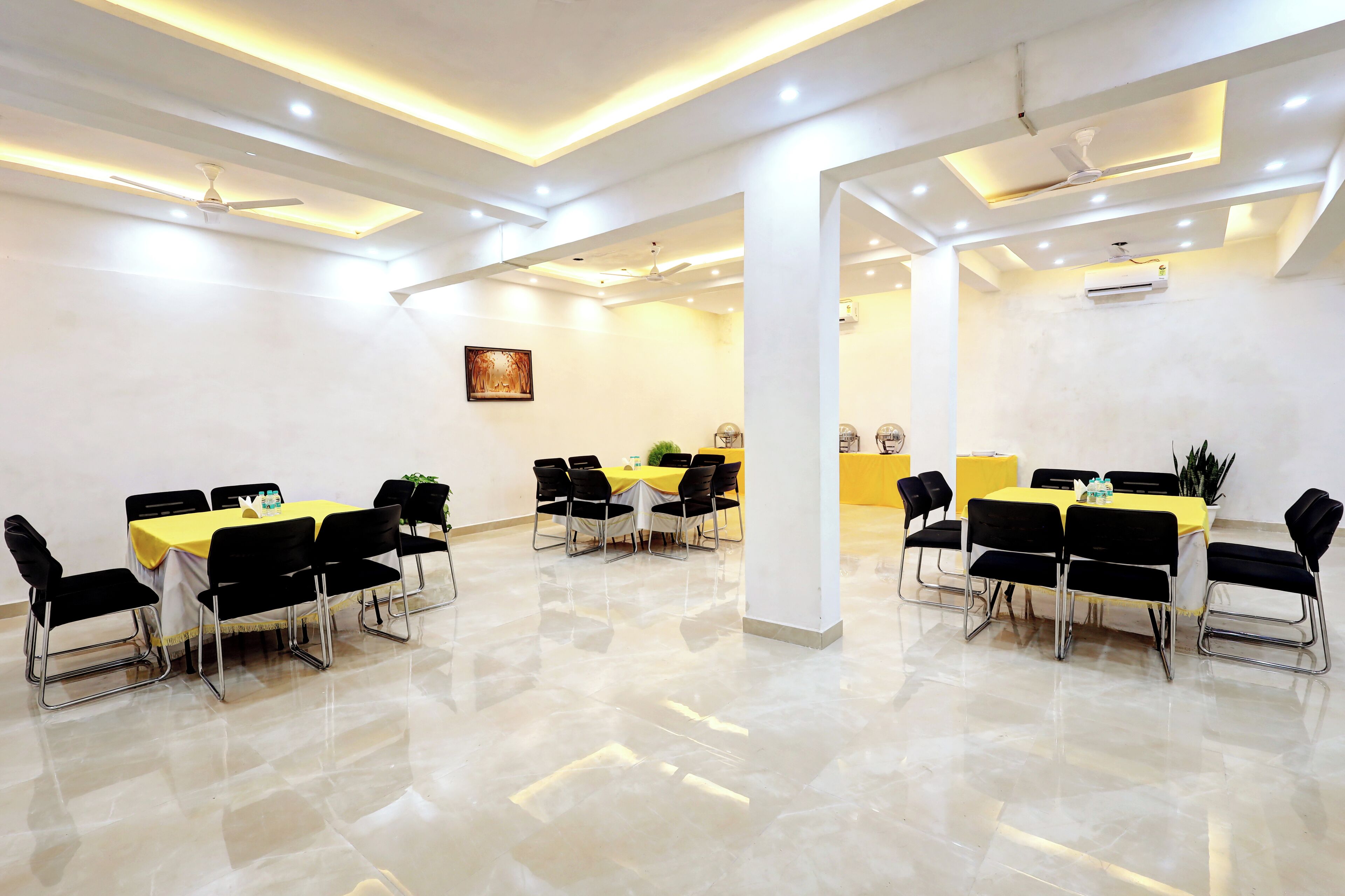 A conference room with two tables, each surrounded by black chairs, and a ceiling fan above.