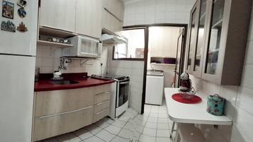 A compact kitchen with white cabinets, a red countertop, a microwave, a stove, and a small refrigerator.