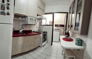 A compact kitchen with white cabinets, a red countertop, a microwave, a stove, and a small refrigerator.