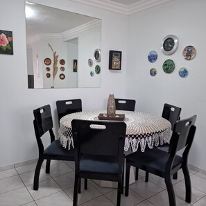 Een eetgedeelte met een ronde tafel, bedekt met een witte kantkleed, omringd door vier zwarte stoelen.