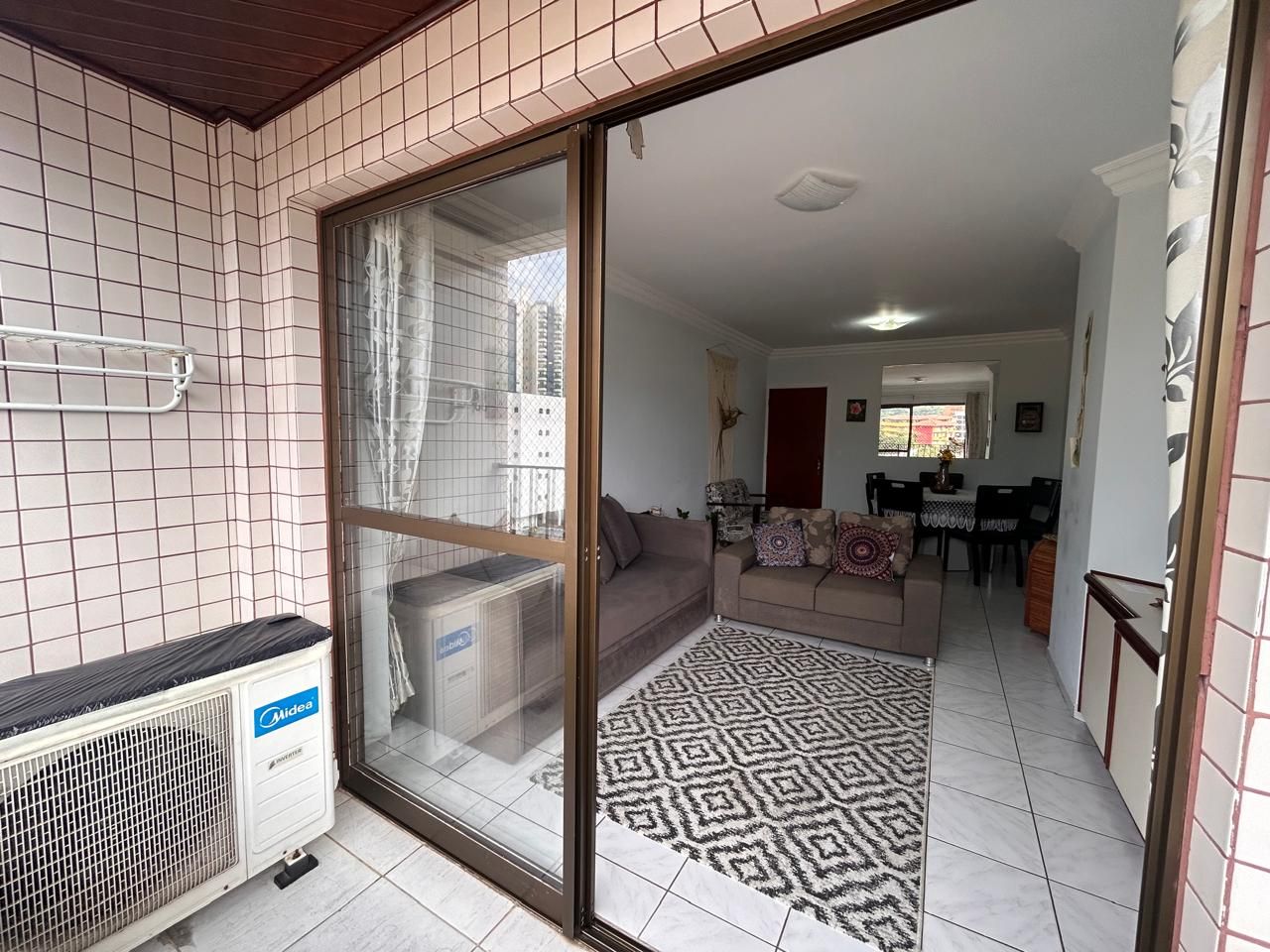 A residential interior with a sliding glass door leading to a living area, a patterned rug, and a white tiled floor.