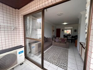 A residential interior with a sliding glass door leading to a living area, a patterned rug, and a white tiled floor.