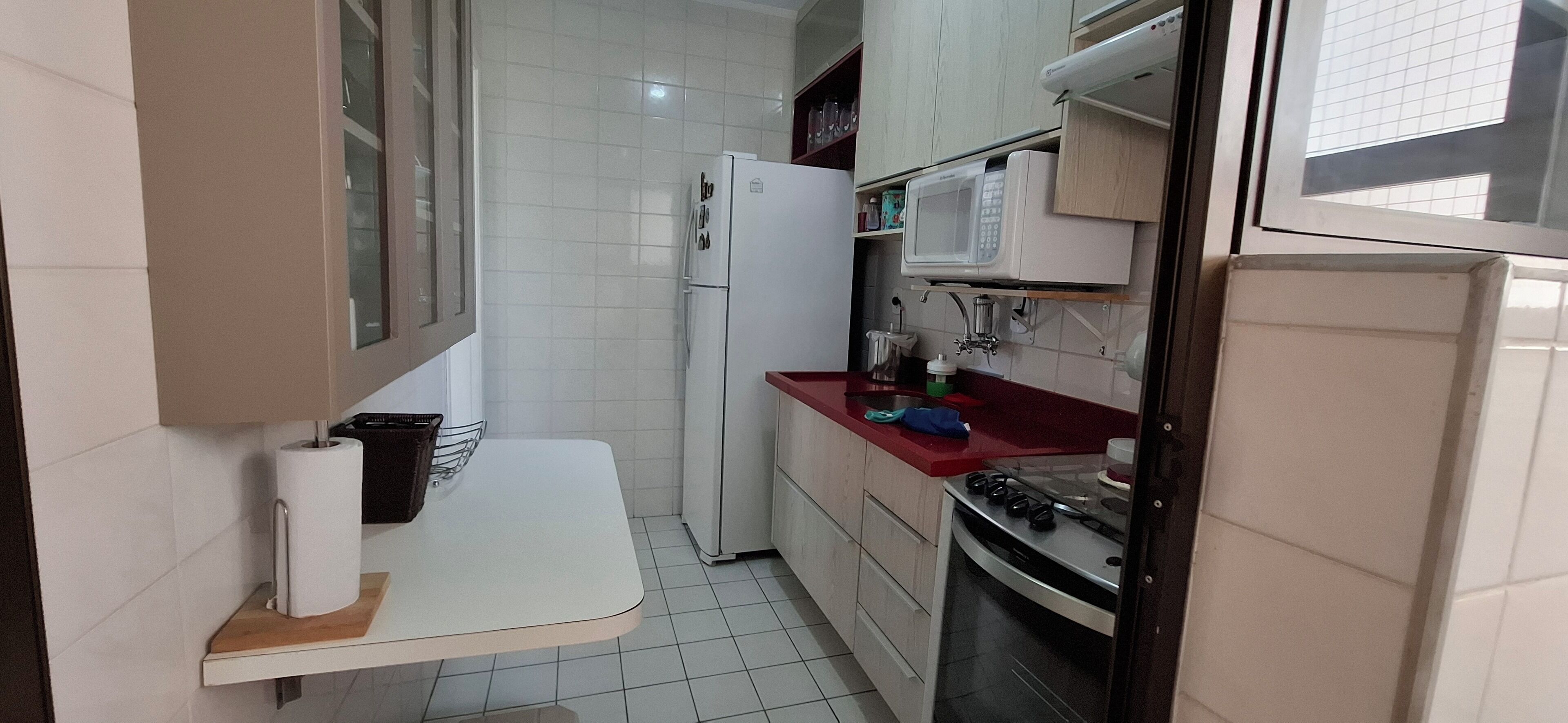Una cocina compacta con armarios blancos, un microondas, un refrigerador y una estufa.