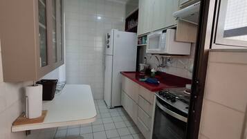 Una cocina compacta con armarios blancos, un microondas, un refrigerador y una estufa.