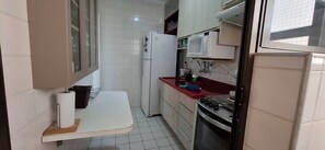 Een kleine keuken met witte kastjes, een magnetron, een koelkast en een fornuis.