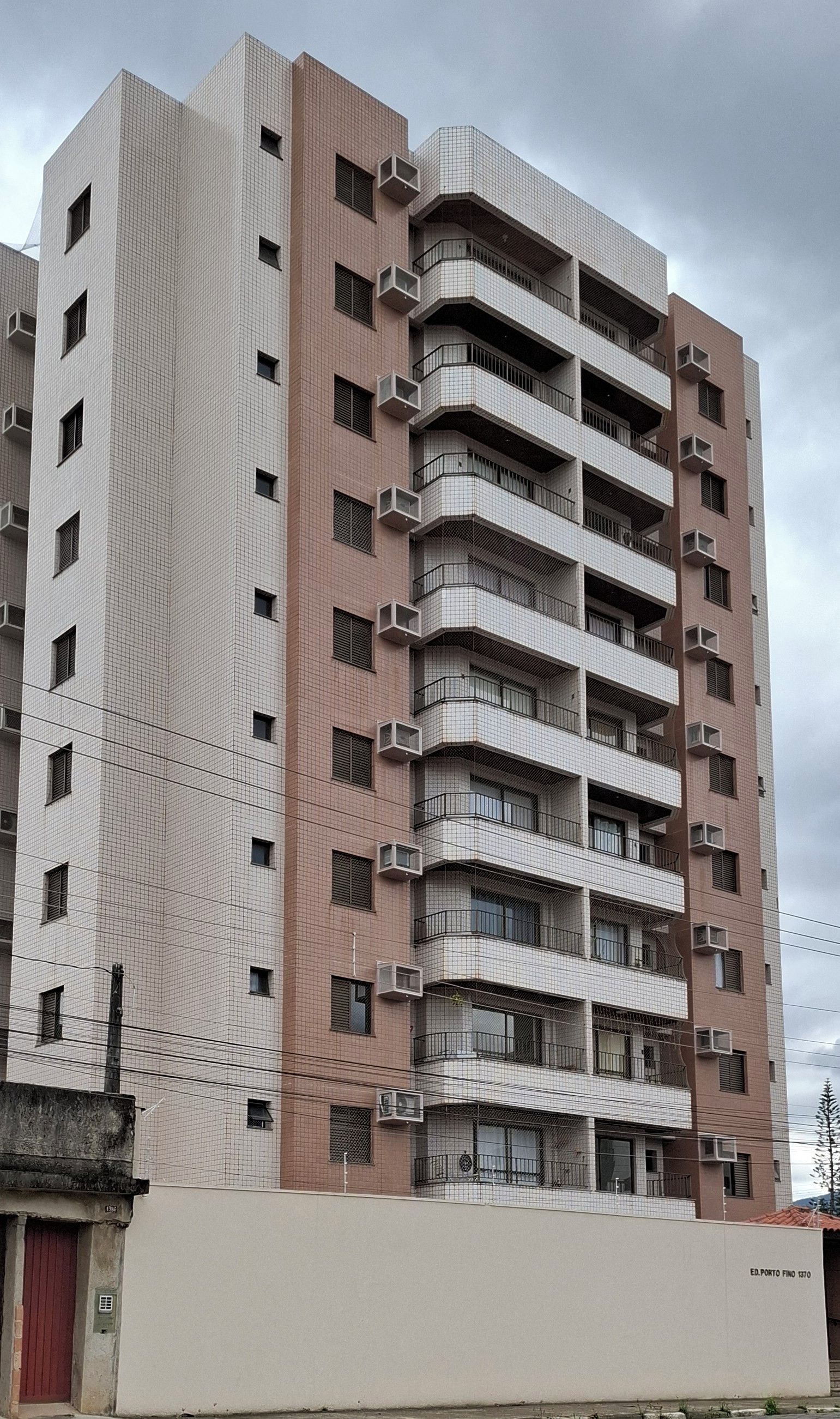 Um edifício residencial de vários andares com fachada uniforme, sacadas e aparelhos de ar condicionado.