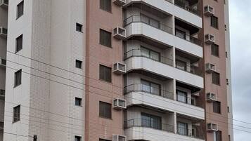 Um edifício residencial de vários andares com fachada uniforme, sacadas e aparelhos de ar condicionado.
