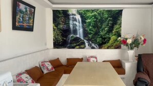 Una habitación con un amplio mural de cascada, una mesa de comedor y un sofá con cojines estampados.