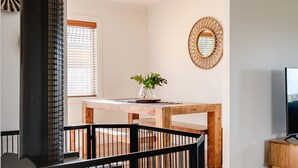 Una habitación con una mesa de comedor de madera, una barandilla negra, un espejo grande y un televisor sobre un mueble de madera.