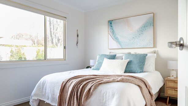 Un dormitorio con una cama, una ventana, una mesita de noche y una obra de arte colgada en la pared.