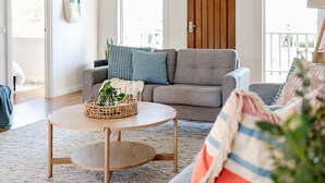 Una sala de estar con un sofá gris, una mesa de centro redonda de madera y una manta a rayas sobre un sofá.