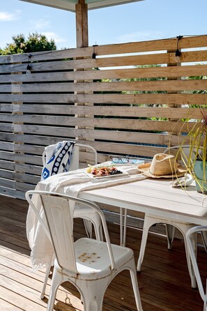 A wooden deck with a white table and chairs, a woven basket, and a plate of food. - Sandy Shores I Town location (Inverloch)