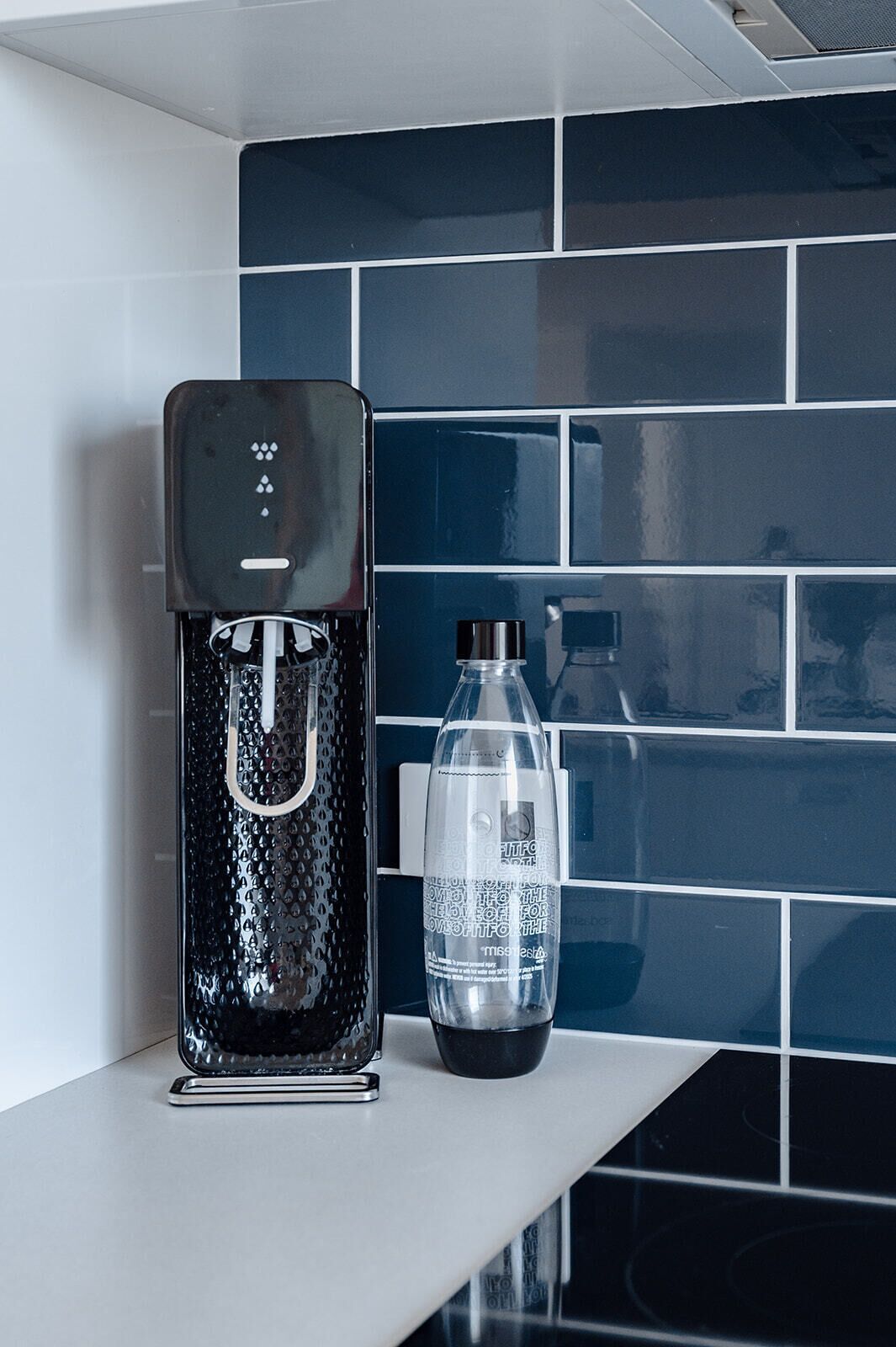 A water dispenser and a bottle on a counter with a tiled backsplash.