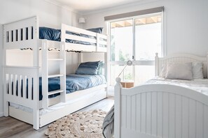 A room with bunk beds, a window with blinds, a bedside lamp, and a woven rug. - Sandy Shores I Town location (Inverloch)