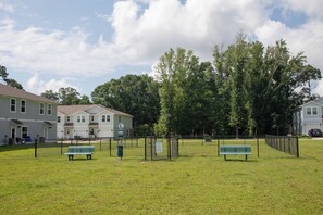 Un espacio al aire libre rodeado por una cerca, con dos bancos verdes, una reja y un edificio al fondo.