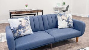 A modern living room with a blue sofa, a coffee table, and a dining area with a wooden table and chairs.