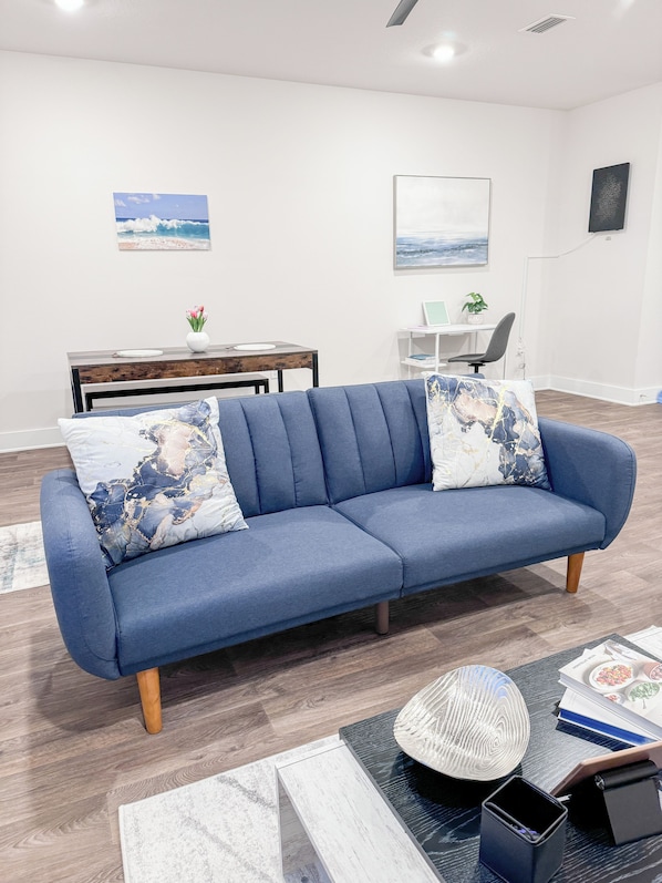 Una sala de estar moderna con un sofá azul, una mesa de centro y un comedor con una mesa y sillas de madera.