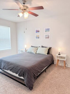 Un dormitorio con cama, ventilador de techo, mesitas de noche y decoración en la pared.