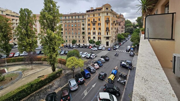 Ein mehrstöckiges Gebäude mit Innenhof, umgeben von parkenden Autos und Bäumen.