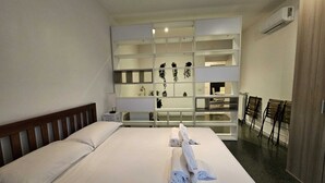 Ein Hotelzimmer mit Bett, Nachttisch in Weiß, einer Wandablage mit Pflanzen und einer Sitzecke mit Sesseln.