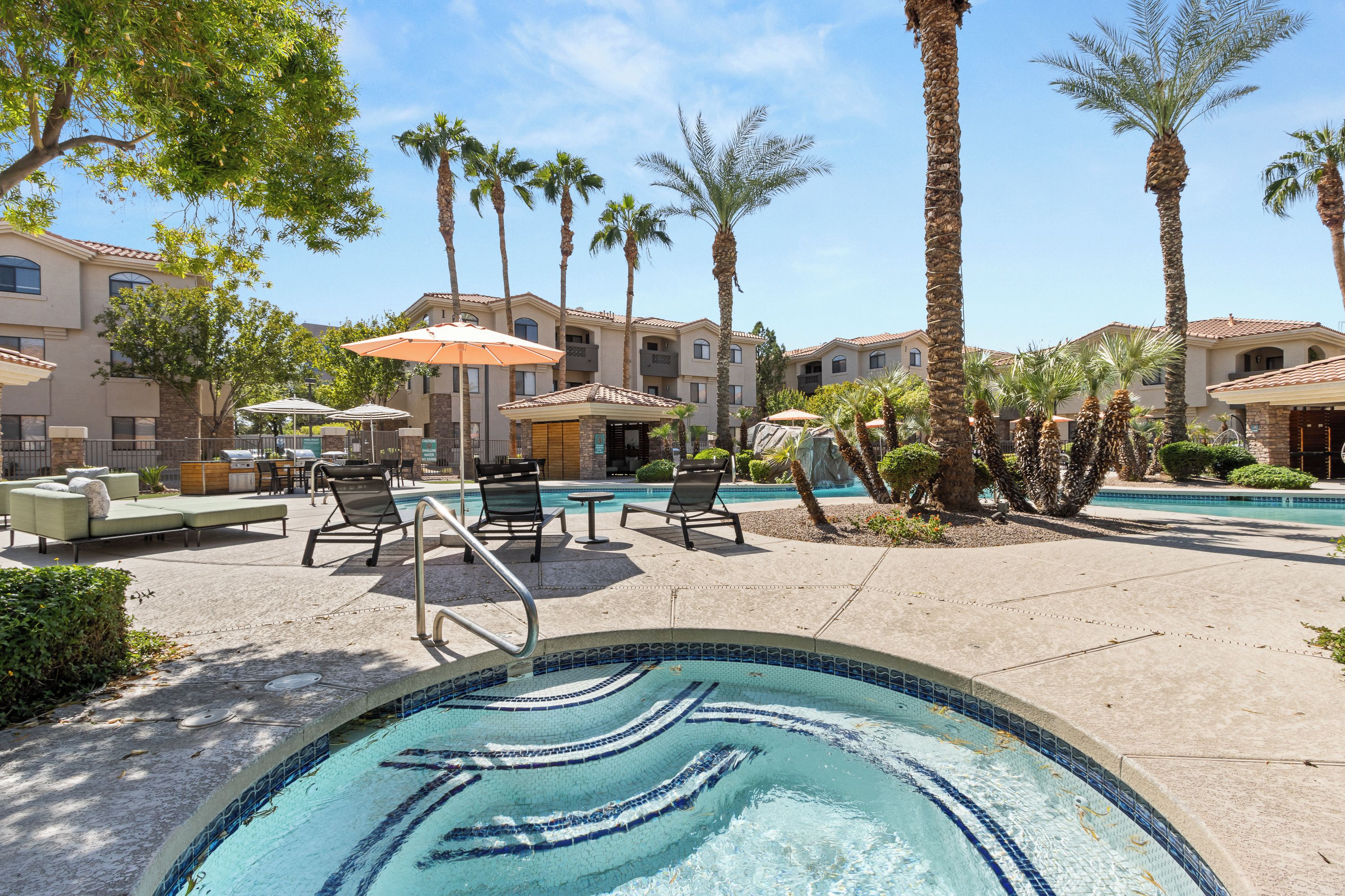 A pool area with lounge chairs, umbrellas, and a clear blue pool.