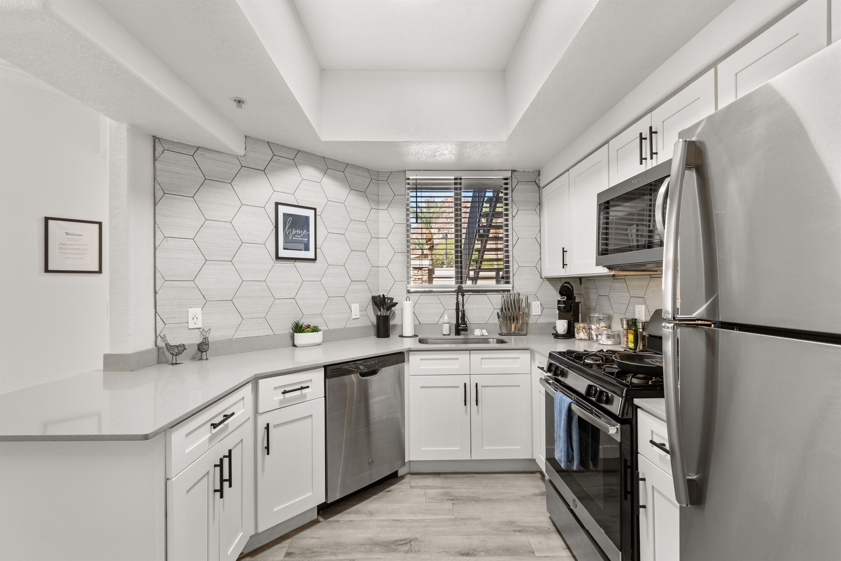 Una cocina moderna con armarios blancos, electrodomésticos de acero inoxidable y un salpicadero de azulejos hexagonales.