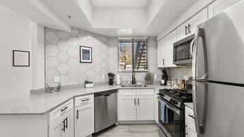 Una cocina moderna con armarios blancos, electrodomésticos de acero inoxidable y un salpicadero de azulejos hexagonales.