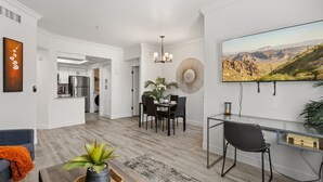 Una sala de estar moderna con comedor, una cocina al fondo y un televisor grande montado en la pared.