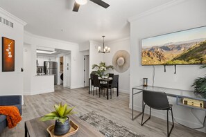 A modern living room with a dining area, a kitchen in the background, and a large TV mounted on the wall.