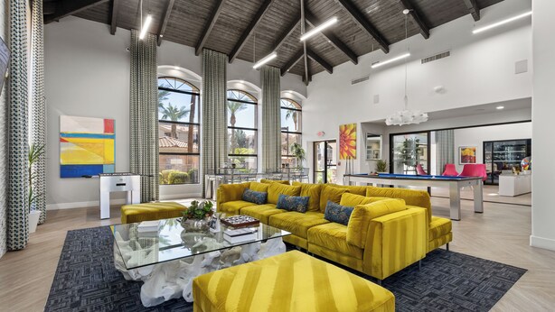 Ampla sala de estar com sofá amarelo, mesa de centro de vidro e mesa de bilhar.