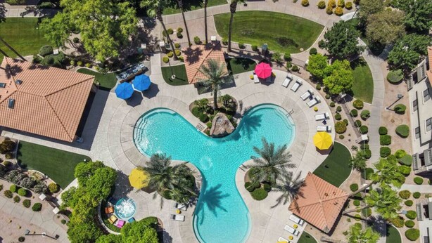 Vista aérea de un complejo turístico con una piscina central, rodeado de palmeras, zonas de descanso y un jardín cuidado.