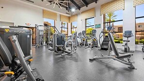 Un gimnasio con diversas máquinas de ejercicio, ventanas amplias y un techo con diseño geométrico.
