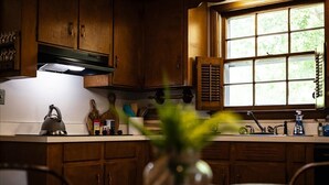 A kitchen with wooden cabinets, a window with blinds, a kettle, and a plant in a vase. - 5BR Woodland Retreat Kayak Fish Pond Rest (North Augusta)