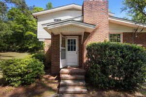 A house with a brick exterior, a white front door, and a small porch with steps leading up to it.