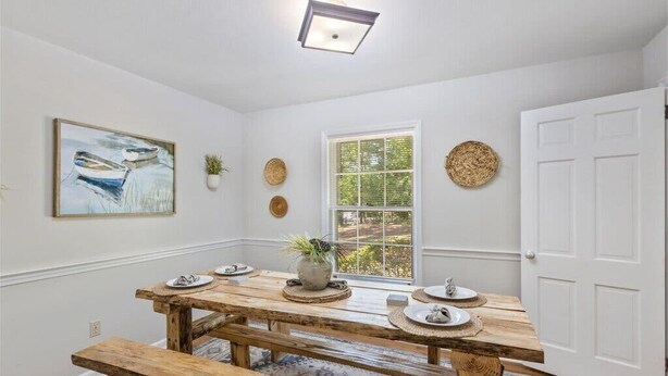 A dining area with a wooden table and benches, a window with a view, and decorative wall art. - 5BR Woodland Retreat Kayak Fish Pond Rest (North Augusta)