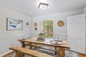 Un comedor con mesa y bancos de madera, ventana con vistas y decoración en la pared.