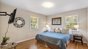 A bedroom with a bed, two windows, a wall-mounted TV, a lamp, and a small table with a plant. - 5BR Woodland Retreat Kayak Fish Pond Rest (North Augusta)