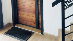 Eine Holztür mit schwarzem Rahmen, eine schwarze Fußmatte und eine Treppe mit schwarzer Geländer.