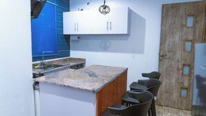 Eine moderne Küche mit Marmorarbeitsplatte, weißen Schränken und einer Wandpaneele aus Holz.