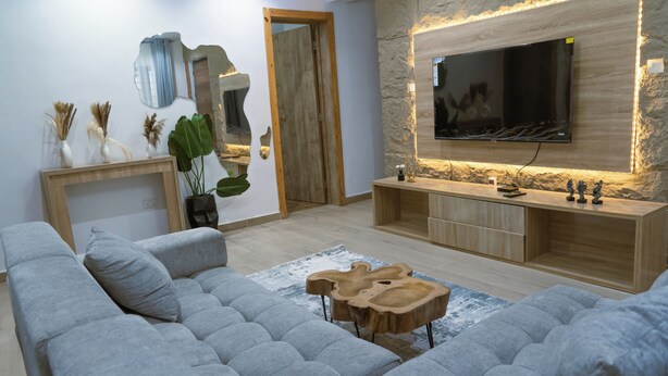 Ein modernes Wohnzimmer mit einem grauen Sofa, einem Holztisch und einem an einer Steinwand befestigten Fernseher.